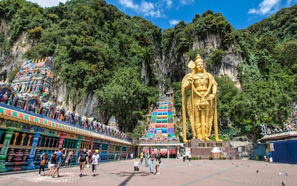 Golden statue and colorful temple at Batu Caves, Malaysia, with tourists exploring the site.