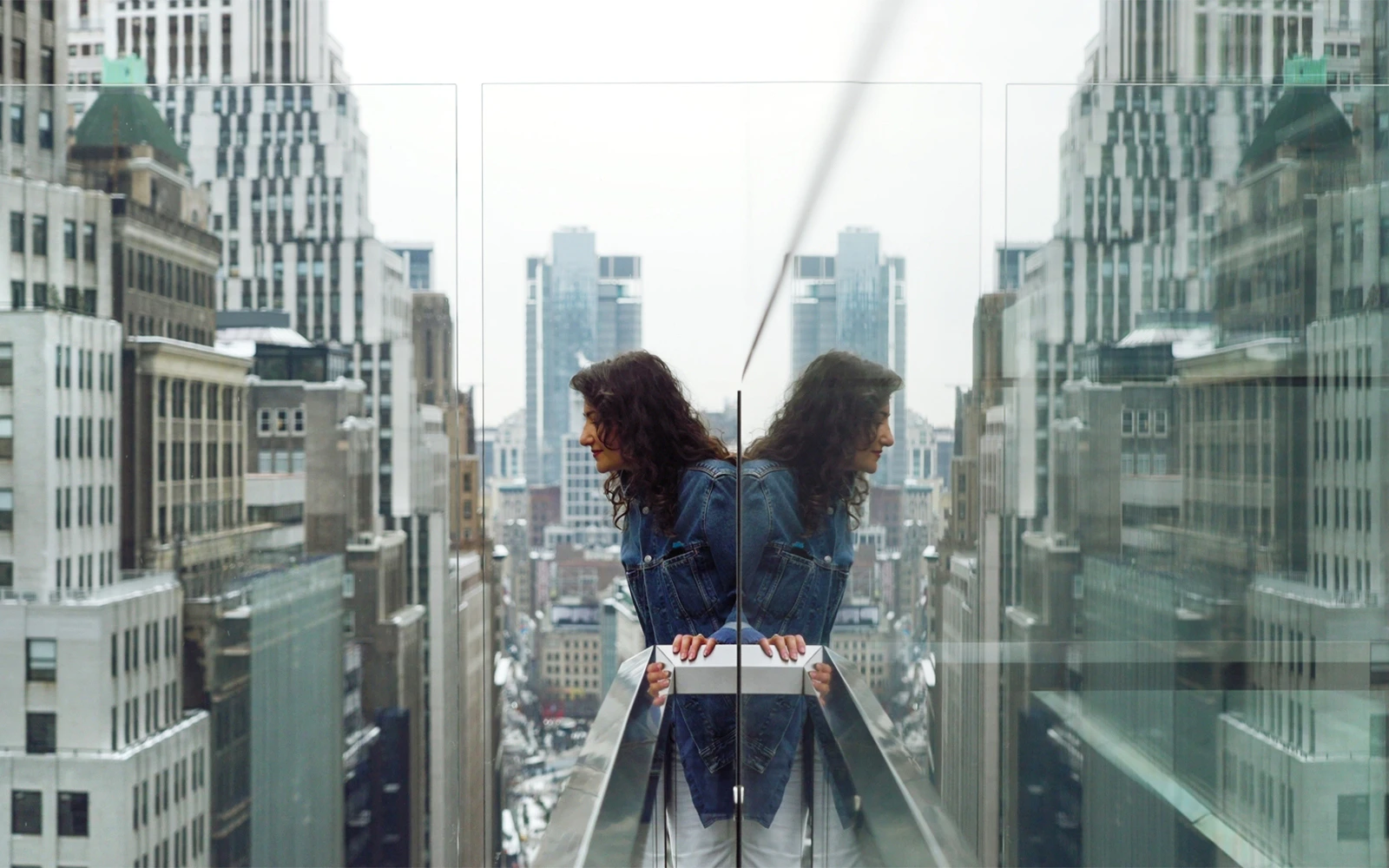 Person looking over the edge of One Times Square Skywalk with cityscape view.