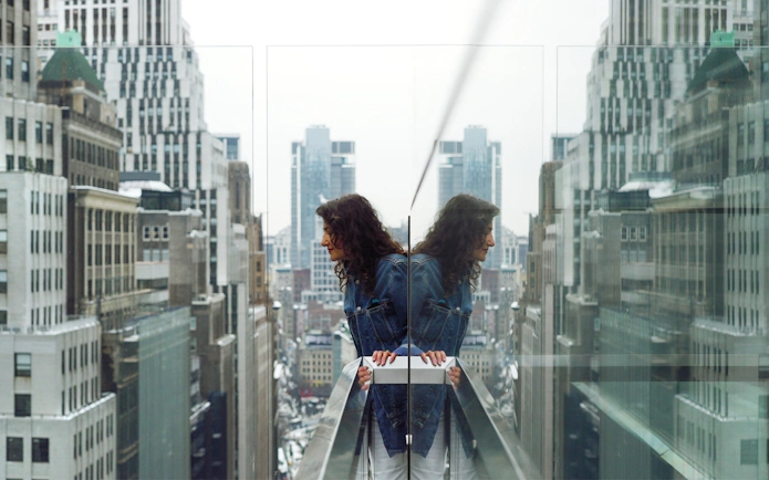 Person looking over the edge of One Times Square Skywalk with cityscape view.