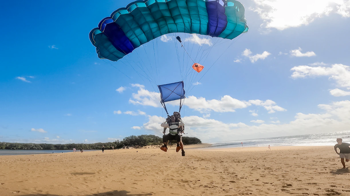Tandem skydive landing on Sunshine Coast beach with parachute open.