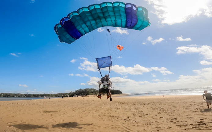 Tandem skydive landing on Sunshine Coast beach with parachute open.