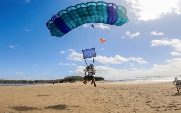 Tandem skydive landing on Sunshine Coast beach with parachute open.
