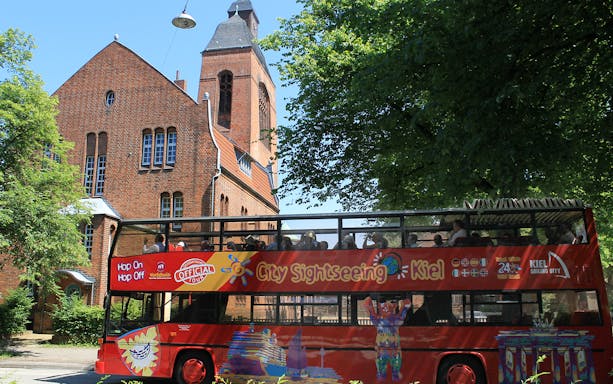Kiel sightseeing bus passing a historic brick church on a sunny day.