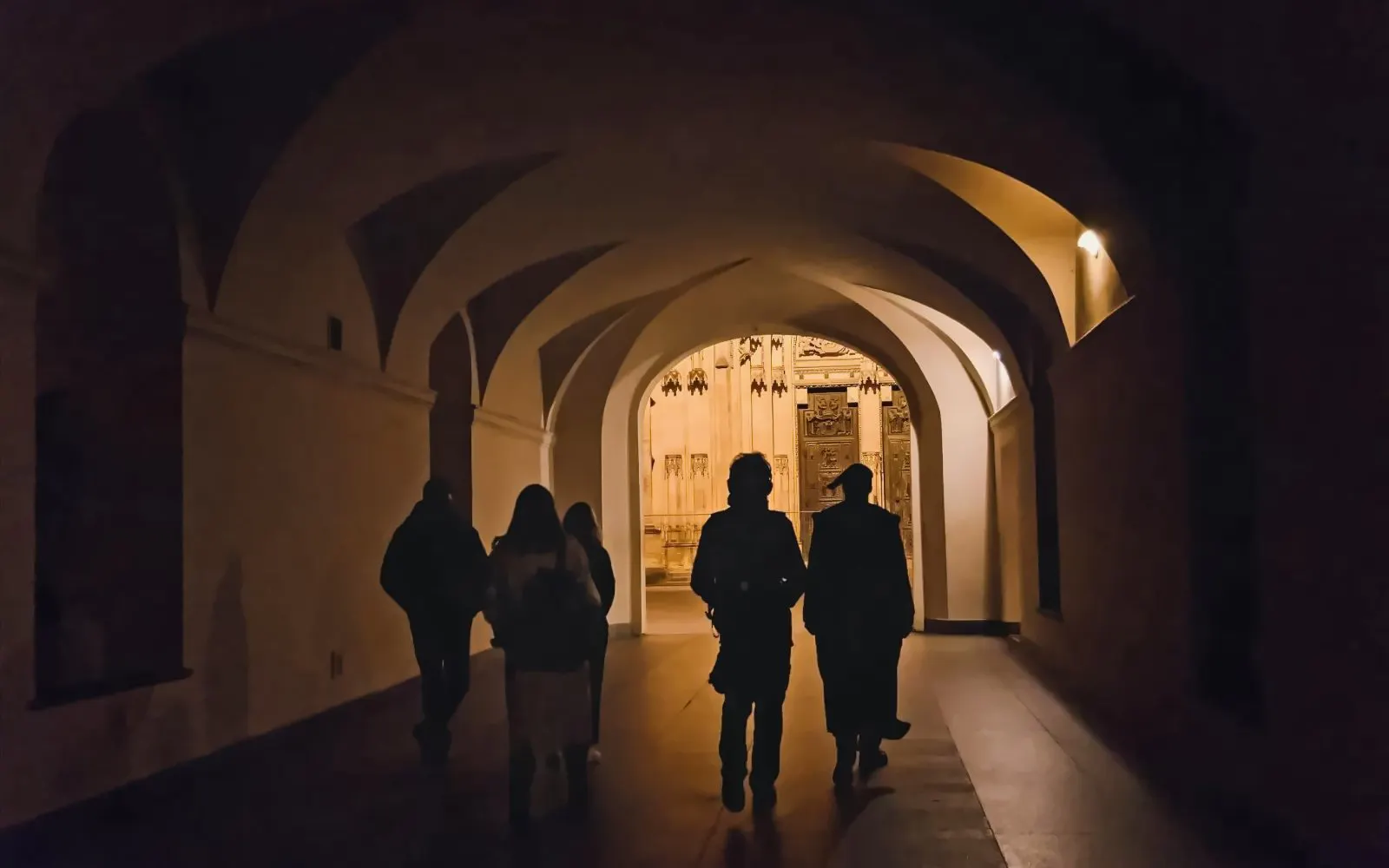 Visitors walking through an illuminated archway at Prague Castle during a guided tour.