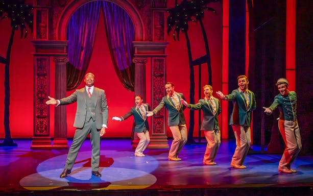 Performers on stage during Pretty Woman The Musical, vibrant red backdrop.