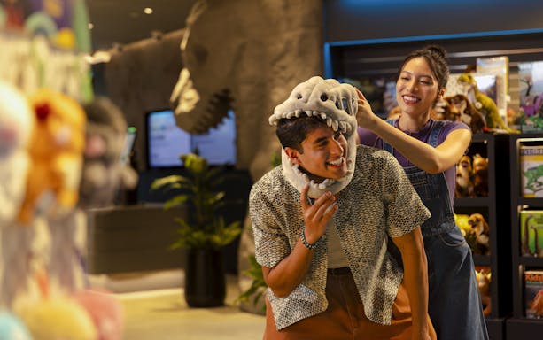Man trying on dinosaur hat at Exploria gift shop, Mandai Wildlife.
