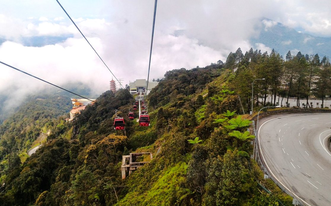 Cable cars ascending over lush mountains with highway view at Genting Highlands, Malaysia.