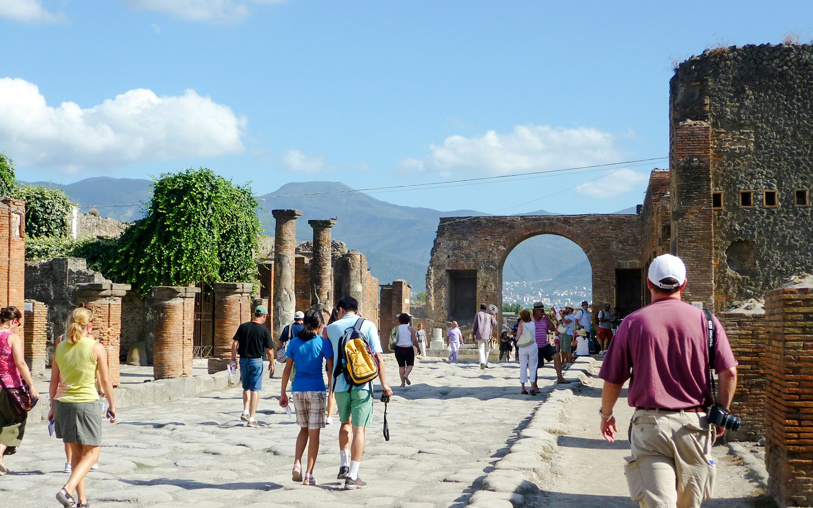 Tourists exploring Pompeii ruins with Mount Vesuvius in the background.