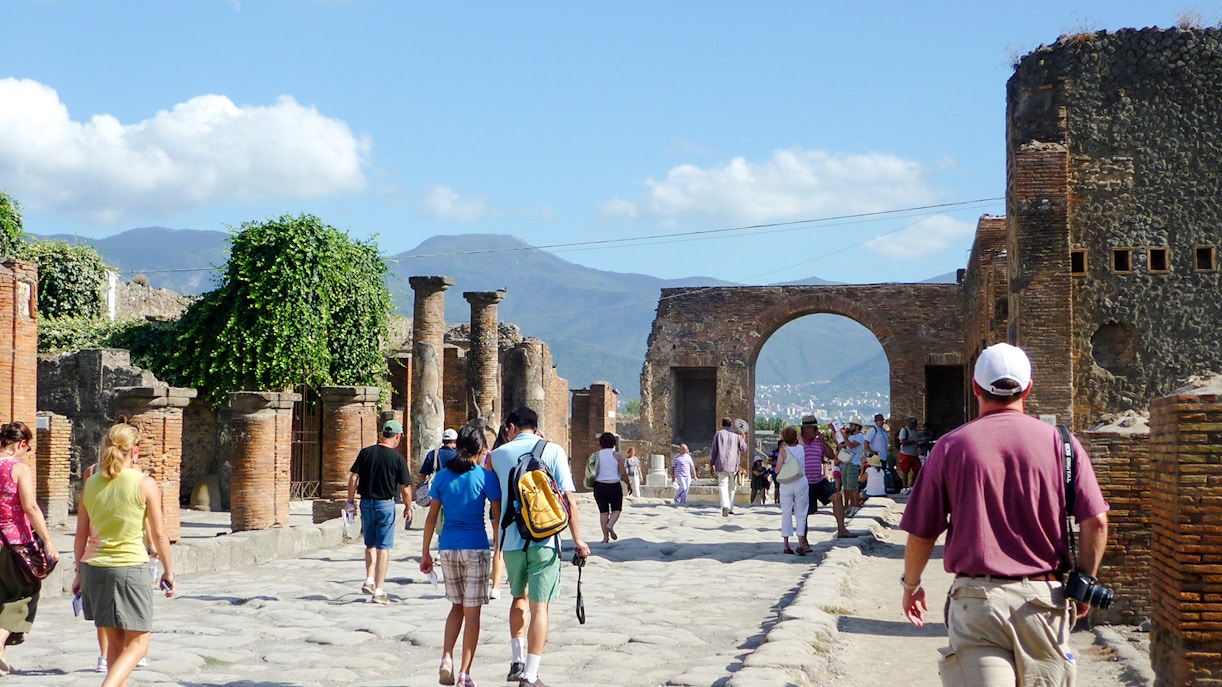 Tourists exploring Pompeii ruins with Mount Vesuvius in the background.