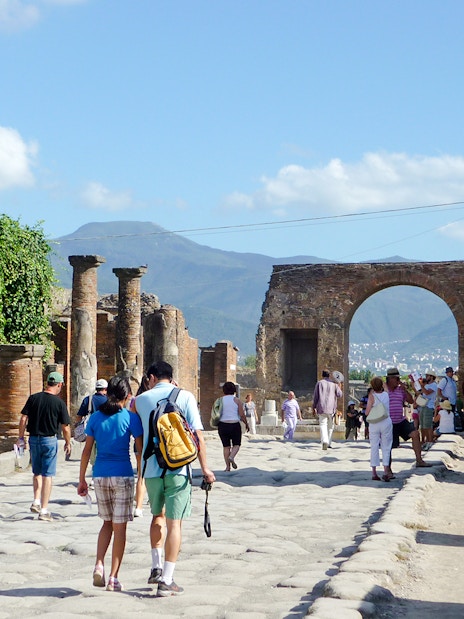 Tourists exploring Pompeii ruins with Mount Vesuvius in the background.