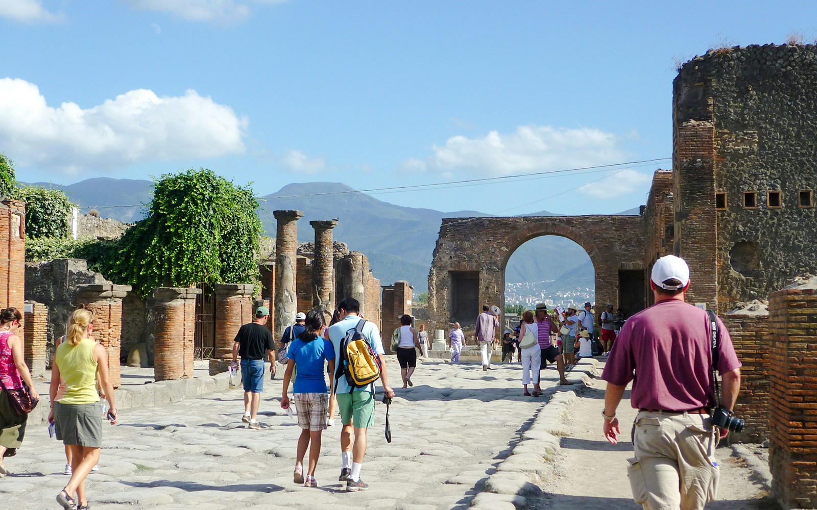 Tourists exploring Pompeii ruins with Mount Vesuvius in the background.