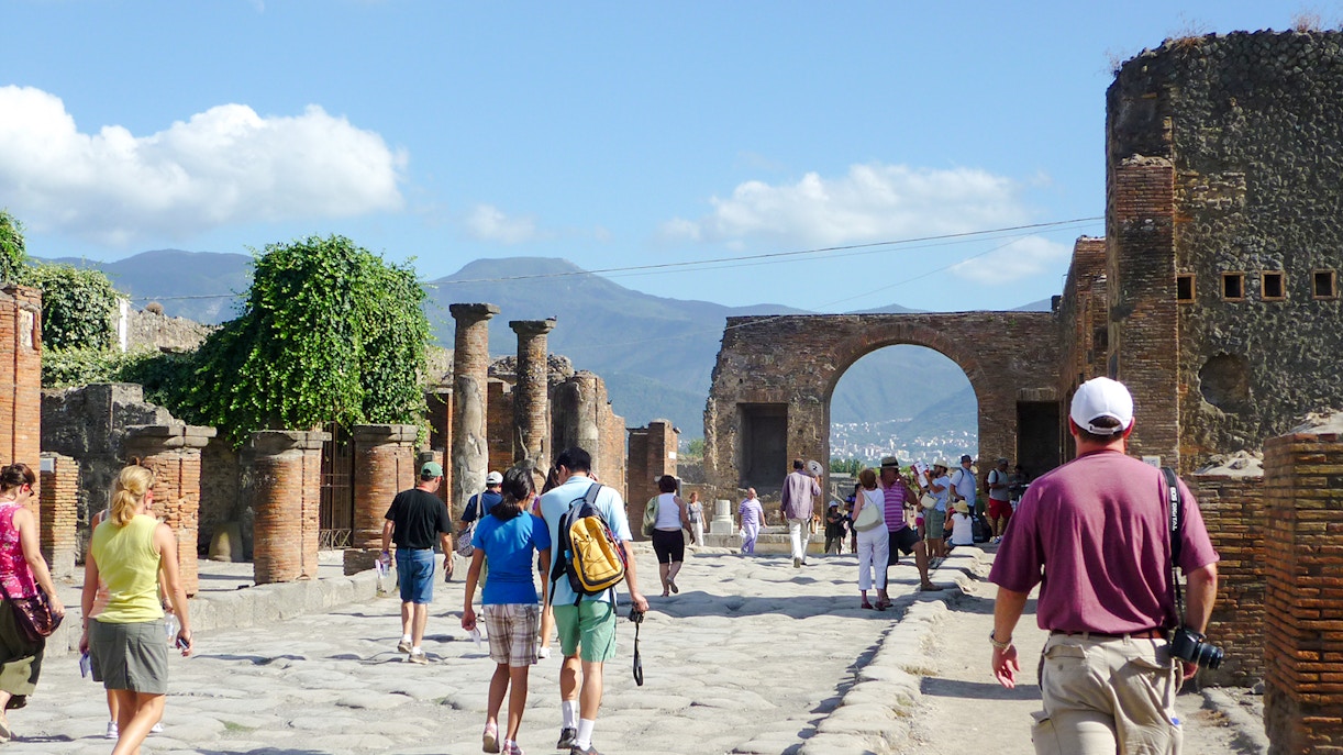 Tourists exploring Pompeii ruins with Mount Vesuvius in the background.