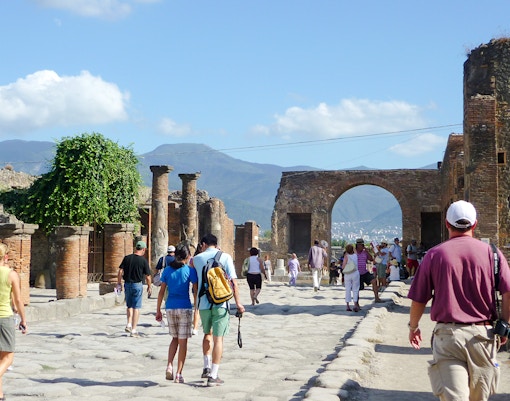 Tourists exploring Pompeii ruins with Mount Vesuvius in the background.