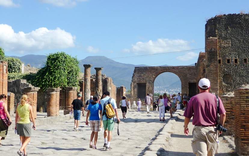 Tourists exploring Pompeii ruins with Mount Vesuvius in the background.