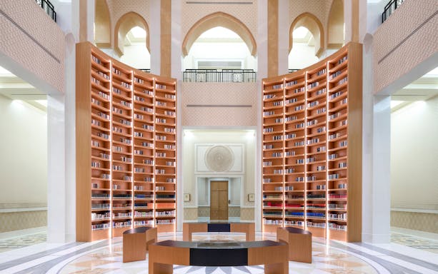 Qasr Al Watan Library interior with tall wooden bookshelves and arched architecture.