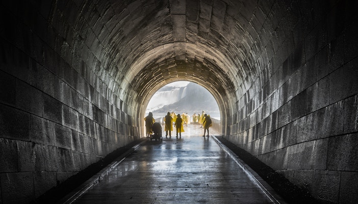 Visitors exploring the Niagara Falls Tunnel with cascading waterfalls in the background.