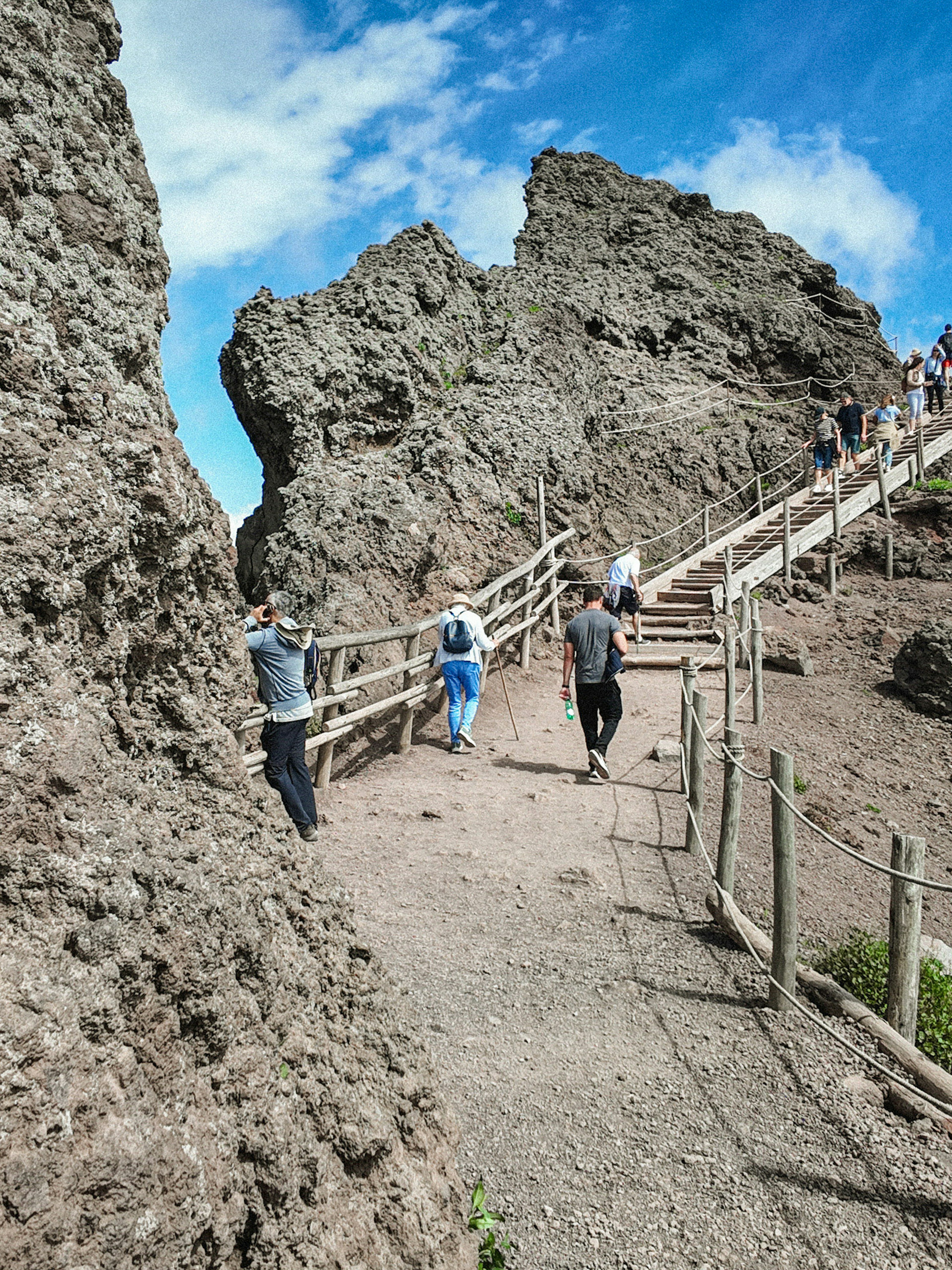 Visitors hiking up the rocky path of Mount Vesuvius under a clear blue sky.