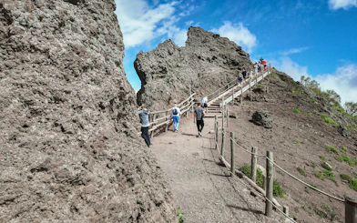 Visitors hiking up the rocky path of Mount Vesuvius under a clear blue sky.