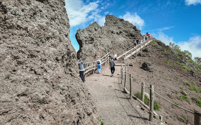 Visitors hiking up the rocky path of Mount Vesuvius under a clear blue sky.