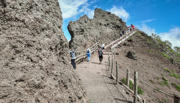 Visitors hiking up the rocky path of Mount Vesuvius under a clear blue sky.
