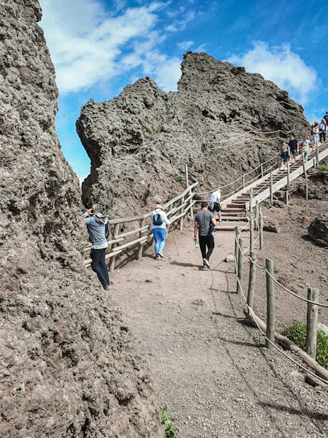 Visitors hiking up the rocky path of Mount Vesuvius under a clear blue sky.