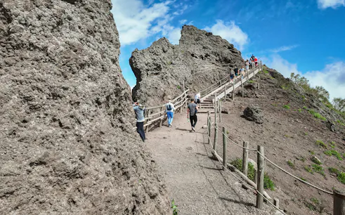 Visitors hiking up the rocky path of Mount Vesuvius under a clear blue sky.