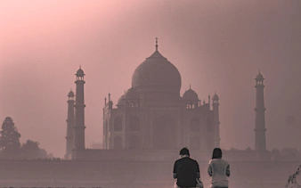 Taj Mahal at sunrise with two visitors in foreground, Agra, India.