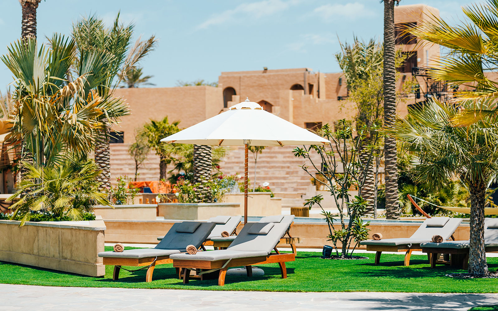 Sun loungers and umbrella at Terra Solis resort with palm trees and desert architecture.
