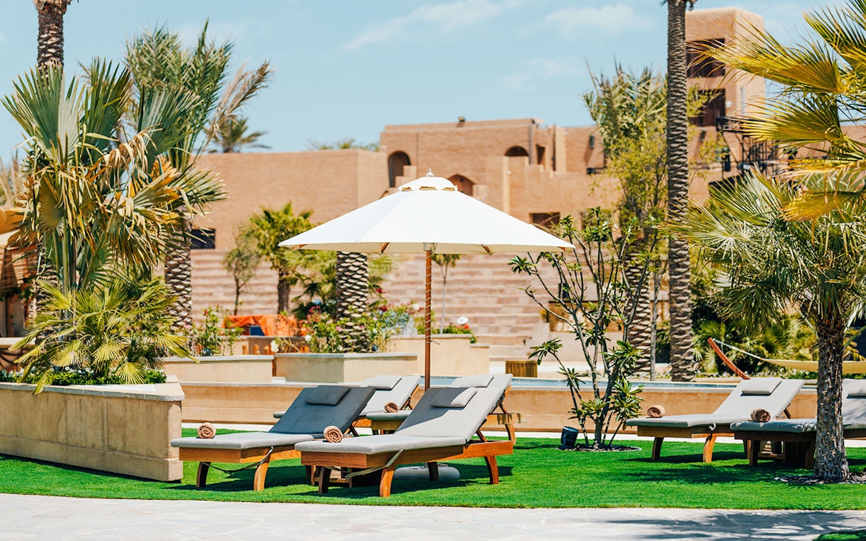 Sun loungers and umbrella at Terra Solis resort with palm trees and desert architecture.
