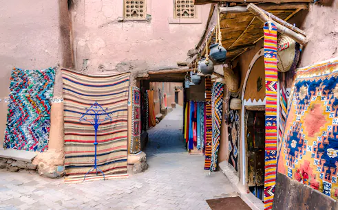 Colorful rugs and pottery in a narrow alley of Marrakesh souk, showcasing local artisan crafts.