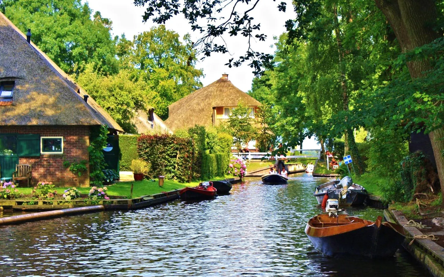 Boats on a canal in Giethoorn with thatched-roof houses and lush greenery.