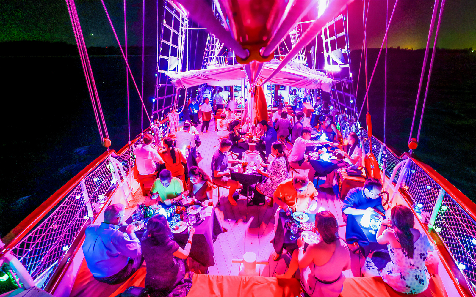 Guests dining on a vibrant evening cruise under colorful lights.