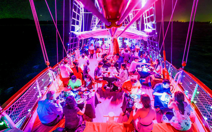 Guests dining on a vibrant evening cruise under colorful lights.