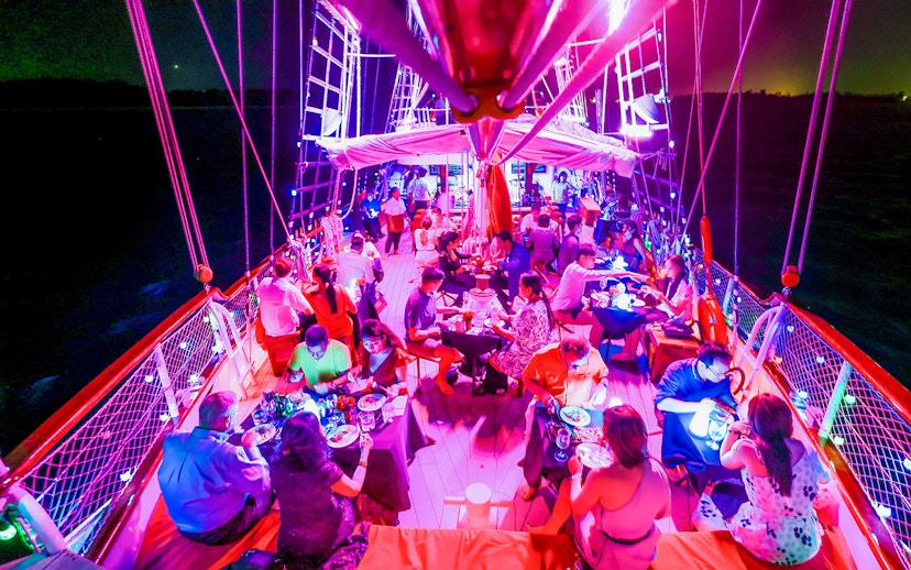 Guests dining on a vibrant evening cruise under colorful lights.
