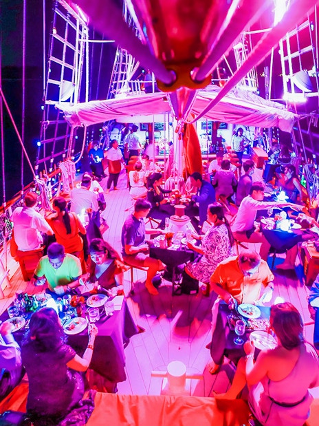 Guests dining on a vibrant evening cruise under colorful lights.