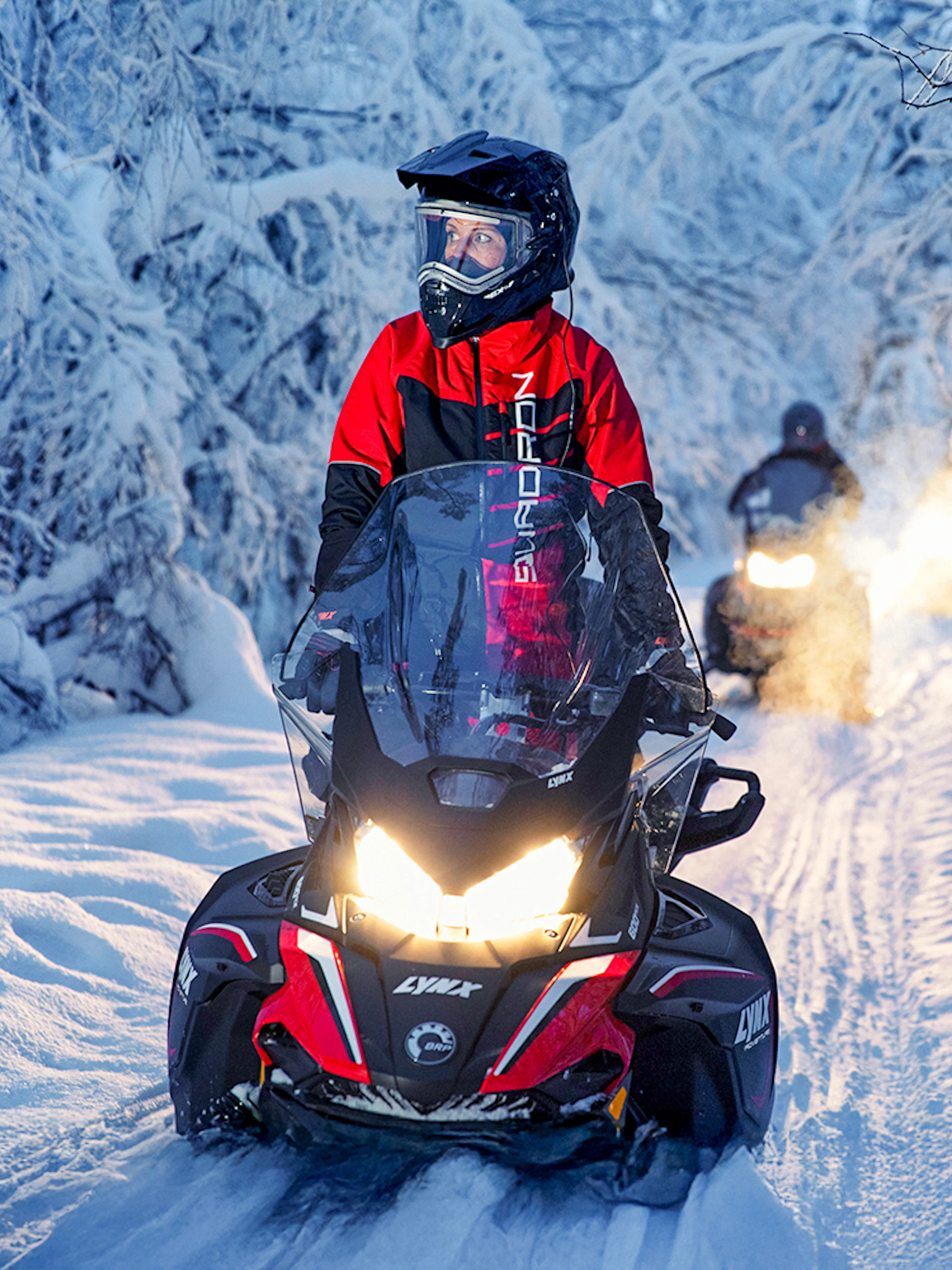 Snowmobile riders on snowy trail during Northern Lights tour.