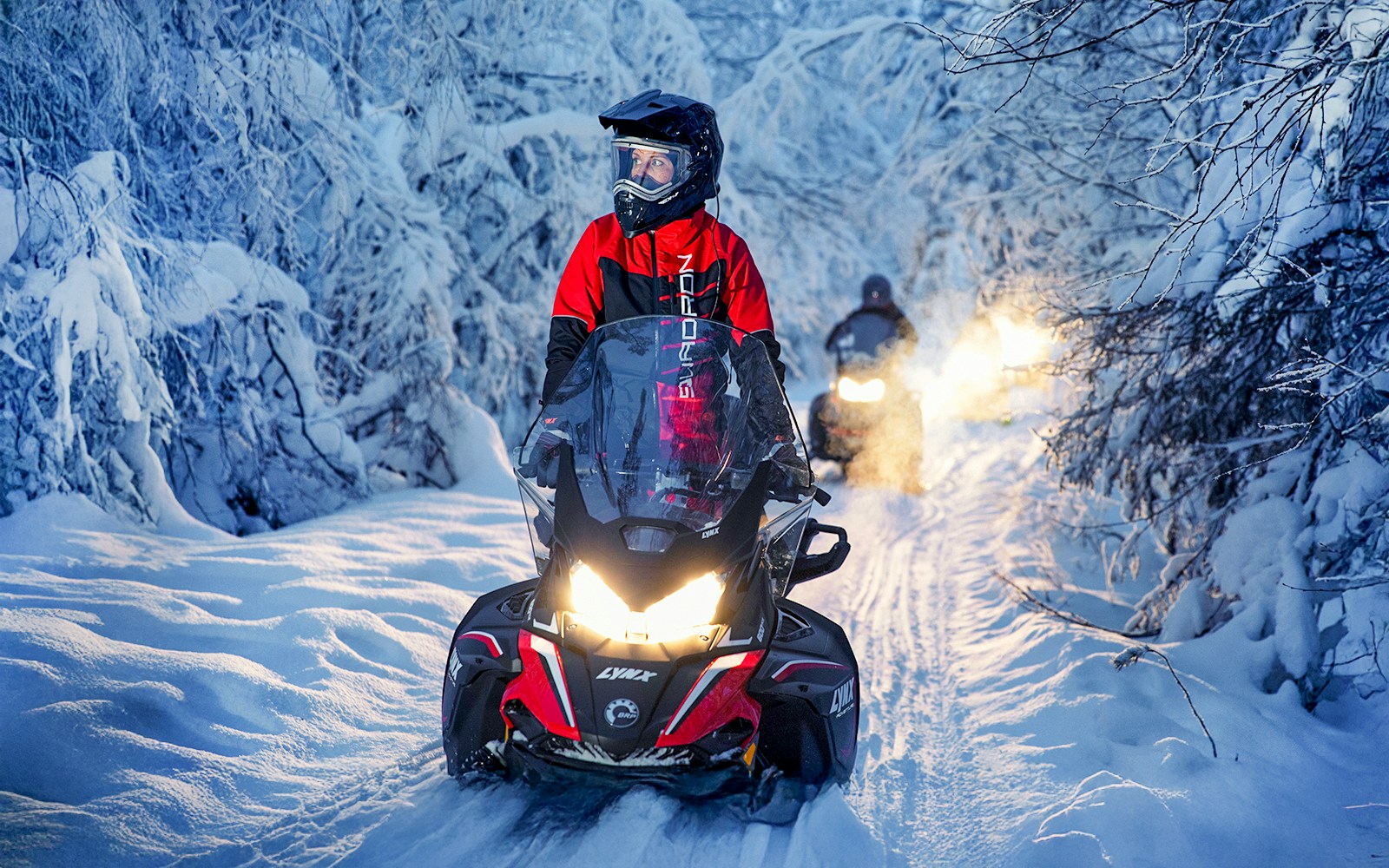 Snowmobile riders on snowy trail during Northern Lights tour.