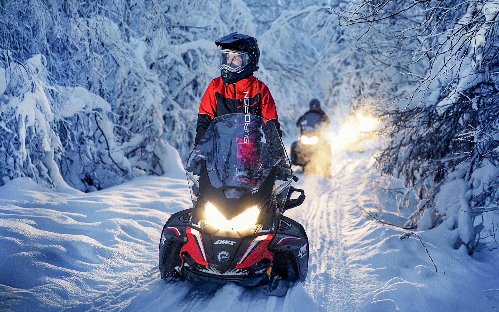 Snowmobile riders on snowy trail during Northern Lights tour.