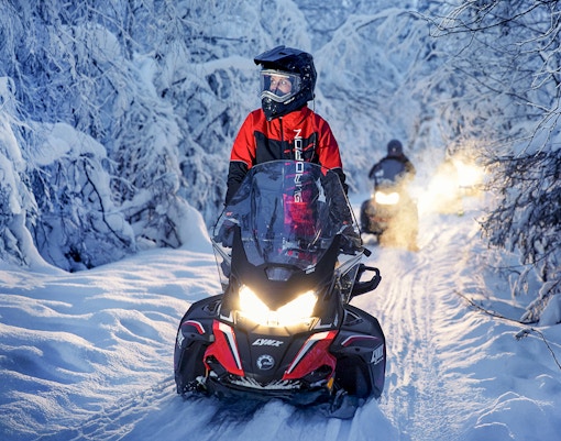 Snowmobile riders on snowy trail during Northern Lights tour.