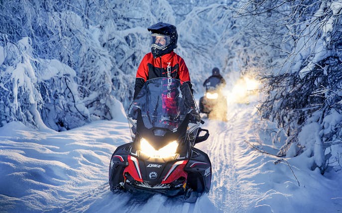 Snowmobile riders on snowy trail during Northern Lights tour.