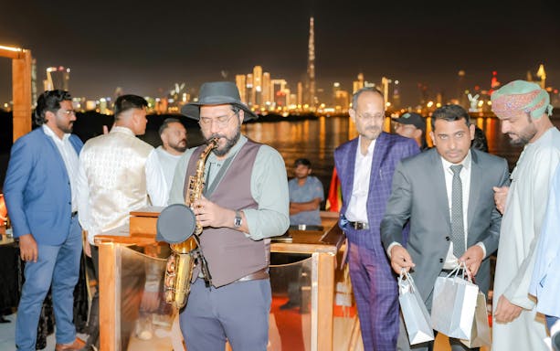 Musician playing saxophone on Dubai Canal dinner cruise with city skyline in background.