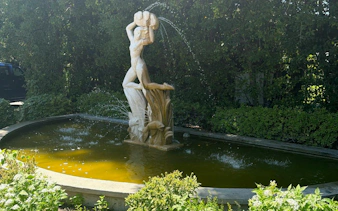 Fountain with a statue of a figure holding a jug, surrounded by greenery in New Orleans.