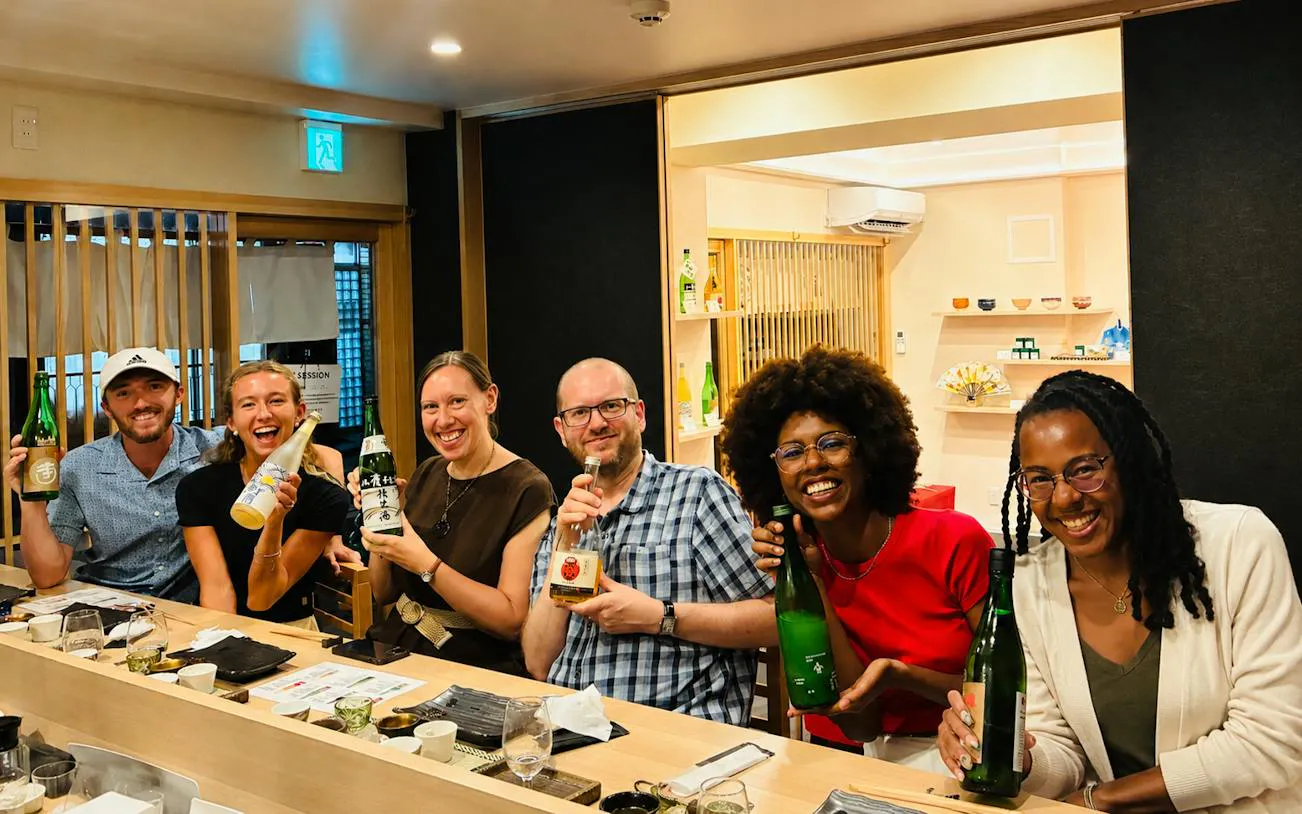 Group enjoying sake tasting with a sommelier in Kyoto, holding various sake bottles.