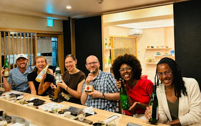 Group enjoying sake tasting with a sommelier in Kyoto, holding various sake bottles.