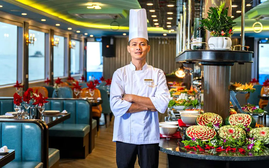 Chef on La Casta Day Cruise in Ha Long Bay dining area with decorative food displays.