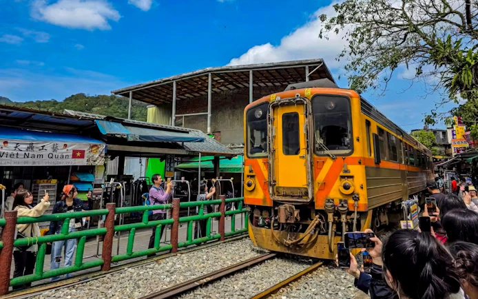 Train passing through Shifen Old Street market in New Taipei City, Taiwan, with visitors taking photos.