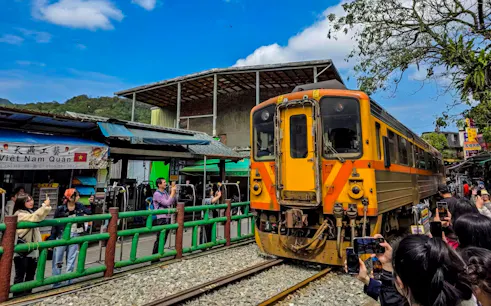 Train passing through Shifen Old Street market in New Taipei City, Taiwan, with visitors taking photos.