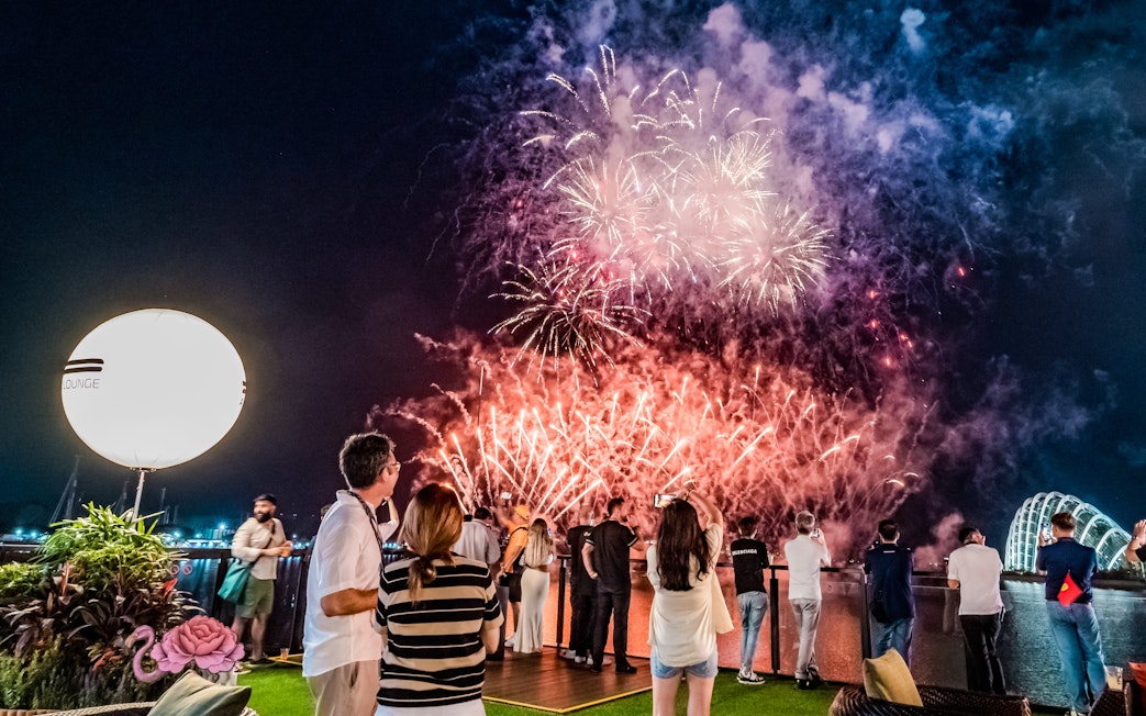 Crowd watching fireworks over Marina Bay, Singapore, celebrating the champion's victory.
