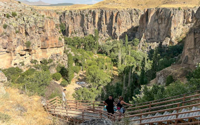 Visitors descending wooden stairs into Ihlara Valley, Cappadocia, surrounded by cliffs and greenery.