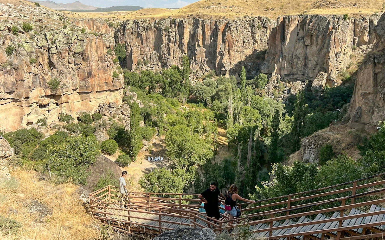 Visitors descending wooden stairs into Ihlara Valley, Cappadocia, surrounded by cliffs and greenery.